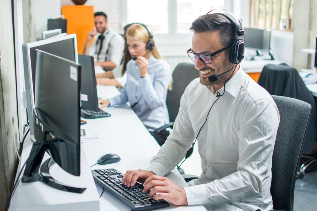 Young male technical support dispatcher with headset talking with customer in call center